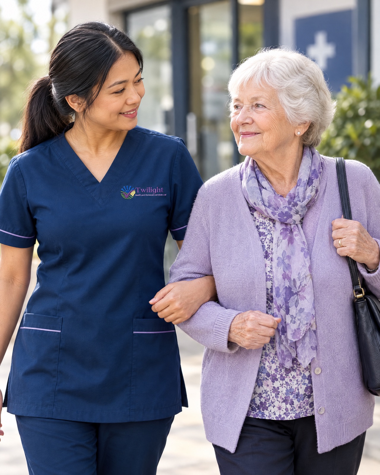 Asian heritage Twilight carer in a twilight-blue uniform accompanying an elderly woman to a clinic appointment in Coventry